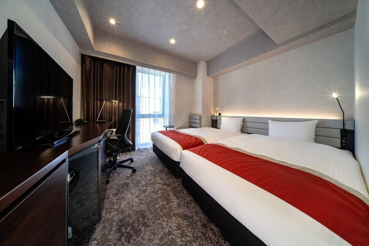 A hotel room with a bed, desk, TV, and a view of the outside.