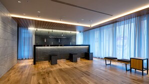 A modern hotel lobby with a reception desk, wooden flooring, and large windows with sheer curtains. - DEL style Ikebukuro Higashiguchi by Daiwa Roynet Hotel (Tokyo)