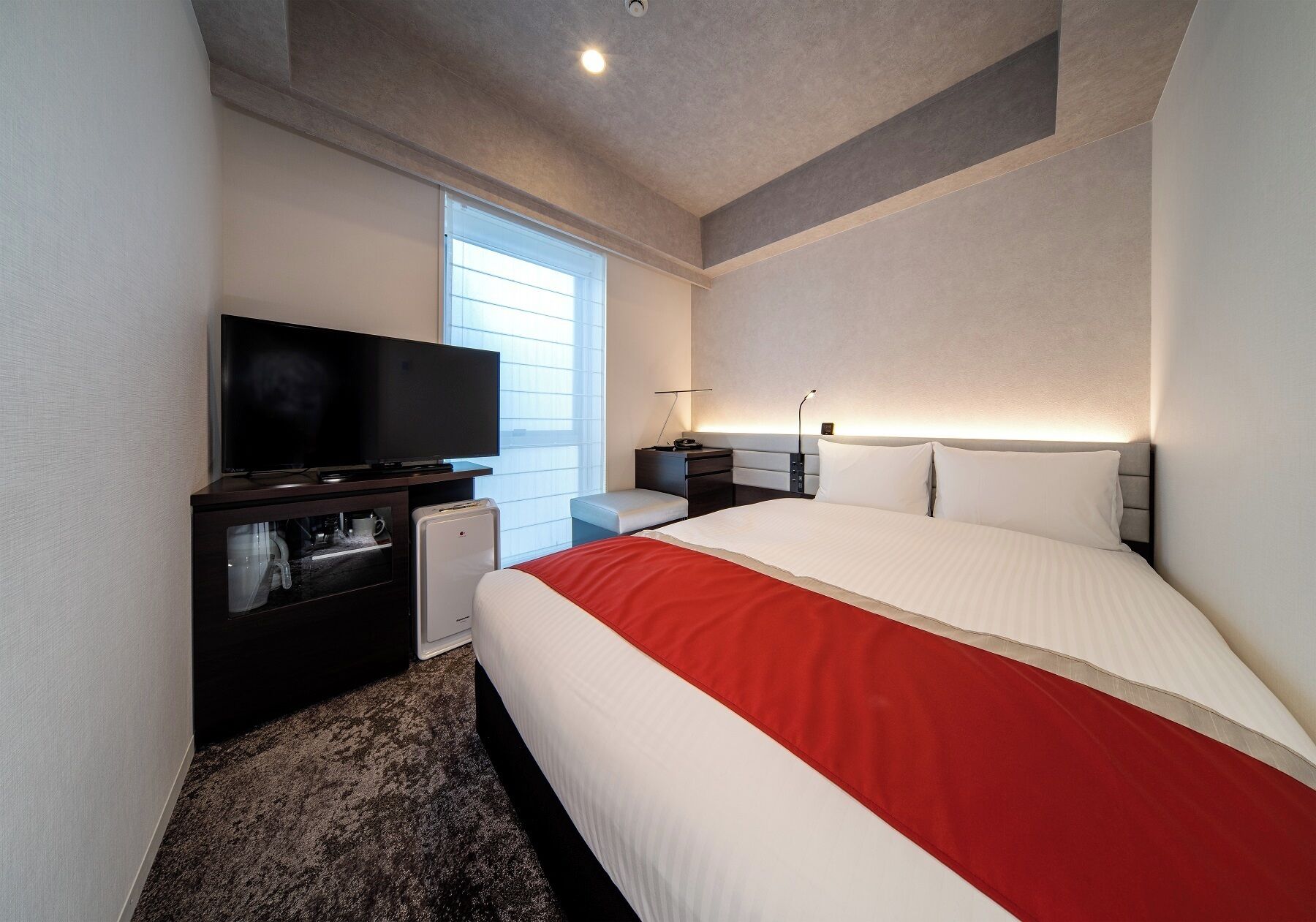 A hotel room with a bed, a television, a desk, and a window.