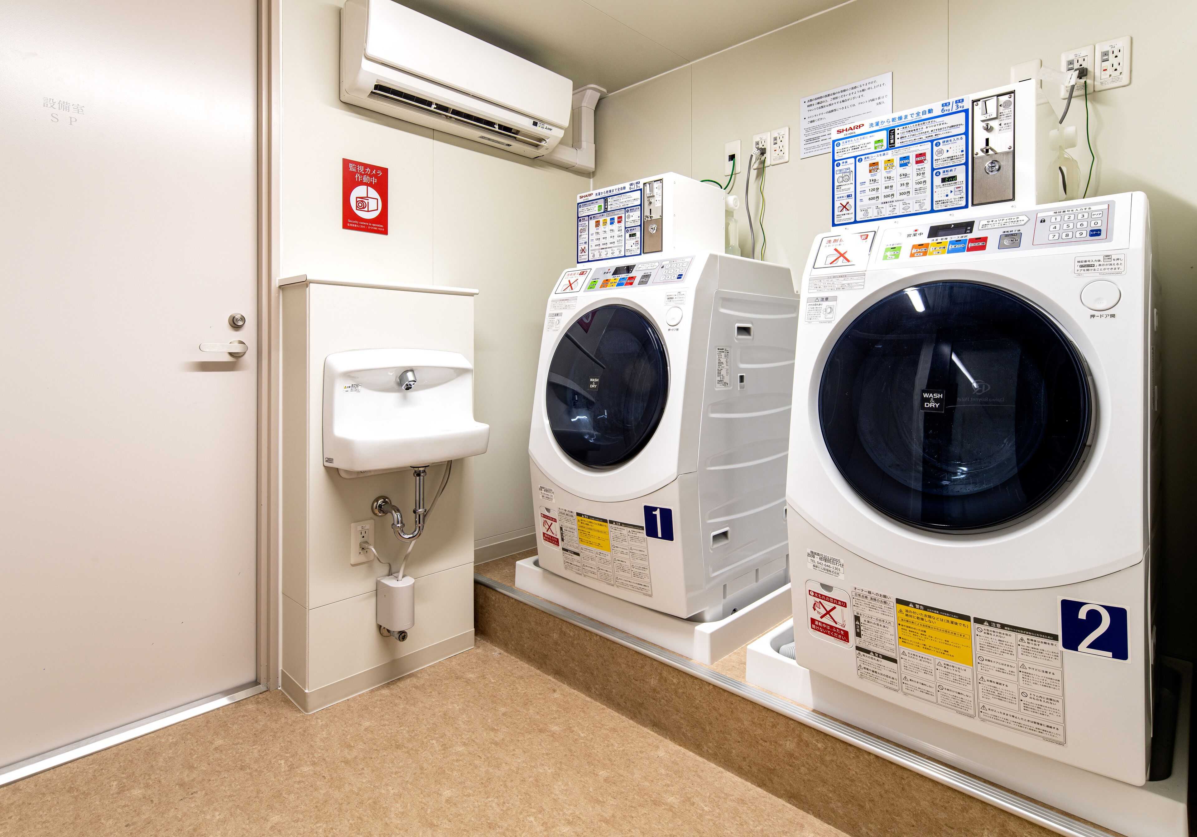 A laundry room with two washing machines, a sink, and a wall-mounted air conditioner.