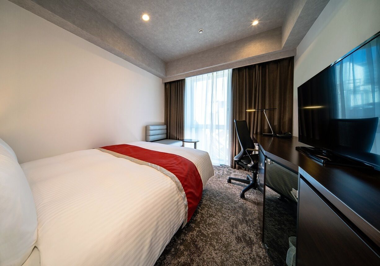 A hotel room with a large bed, a desk with a chair, a television, and a window with curtains.