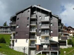 A multi-story residential building with balconies, a stone base, and a clear sky.