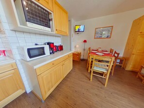 A compact kitchen with a microwave, coffee maker, and a television on the wall.