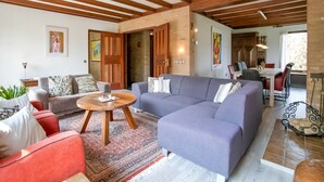 A spacious living room with a large sectional sofa, a round coffee table, and a red armchair. There is a dining area in the background with a table and chairs.