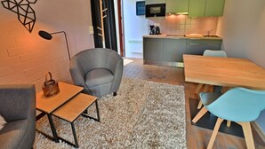 A modern apartment with a grey armchair, a wooden table, a blue chair, and a kitchen with green cabinets. - Apartment in Vielsalm Near Les Doyards Park (Vielsalm)