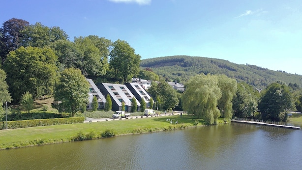 A riverside hotel with modern architecture, a grassy area, and a lake. - Apartment in Vielsalm Near Les Doyards Park (Vielsalm)