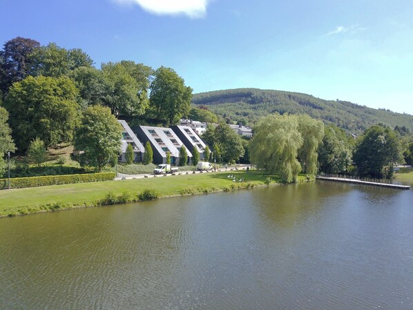 A riverside hotel with modern architecture, a grassy area, and a lake.
