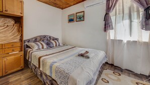 Una camera da letto accogliente con soffitto in legno, un letto con lenzuola decorate, un armadio in legno e una finestra con tende.