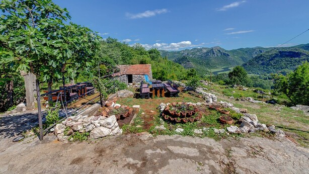 Un edificio rustico in pietra con tetto in tegole rosse, circondato da un vigneto e un paesaggio roccioso.