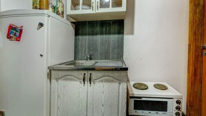 Una cucina compatta con un frigorifero bianco, un forno a microonde e un lavandino. Sopra il lavandino ci sono pensili e una porta in legno sulla destra.