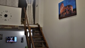 A staircase leading to a higher level, a wall clock, a painting of a historical building, and a television displaying a news program. - casa Del Vicolo (Palermo)