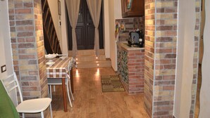 A compact kitchen with a dining area, featuring a brick wall, a small counter with a wine bottle, and a dining table with chairs. - casa Del Vicolo (Palermo)