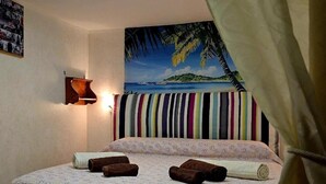 A bed with a patterned bedspread, a wall-mounted lamp, a tropical beach painting, and a striped curtain. - casa Del Vicolo (Palermo)