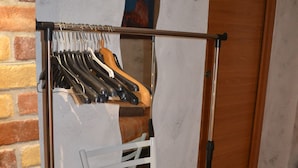 A room with a brick wall, a white chair, a coat rack with hangers, and a wooden door. - casa Del Vicolo (Palermo)