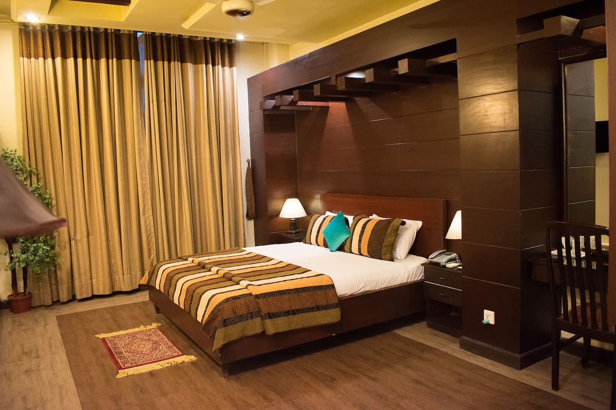 Una habitación de hotel con una cama grande, una mesita de noche, una silla y una planta en maceta.