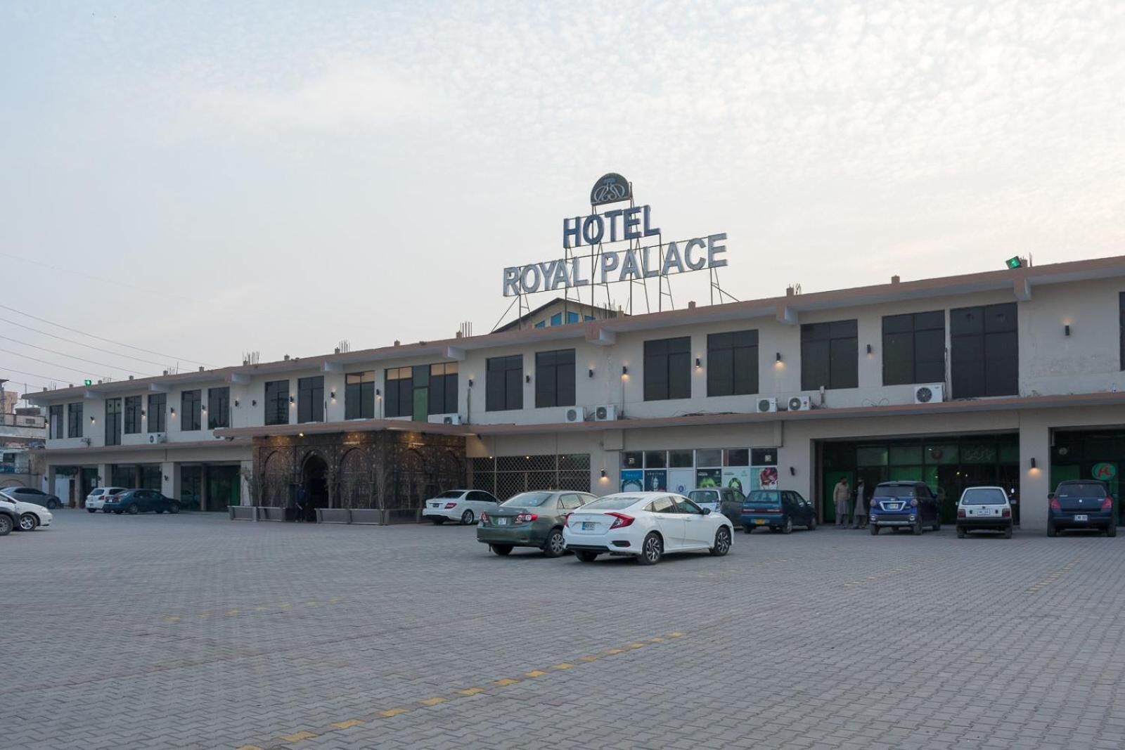 A hotel named Royal Palace with a modern facade, multiple parking spaces, and a clear sky.