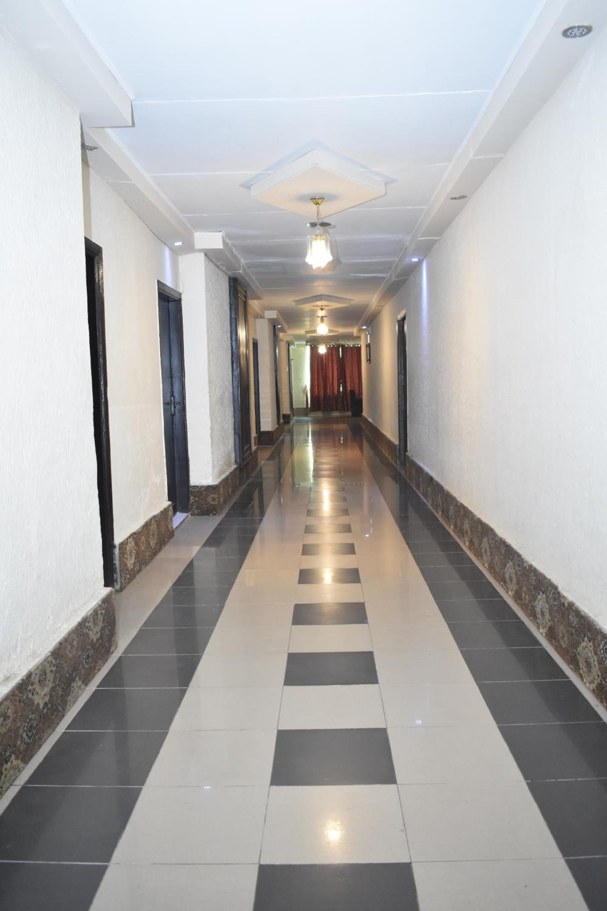 Um corredor comprido e estreito com padrão de piso xadrez, paredes brancas e teto com iluminação embutida e um ventilador.