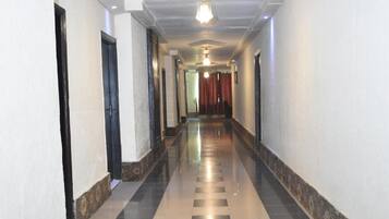 Um corredor comprido e estreito com padrão de piso xadrez, paredes brancas e teto com iluminação embutida e um ventilador.