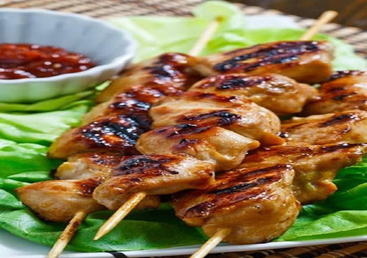 Brochetas de carne a la parrilla sobre hojas de lechuga, acompañadas de un recipiente pequeño con salsa.