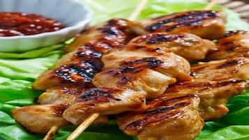 Brochetas de carne a la parrilla sobre hojas de lechuga, acompañadas de un recipiente pequeño con salsa.
