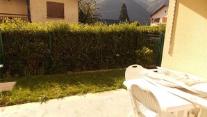 A patio area with a white table and chairs, a hedge, and a mountain view in the background. - Charming 2-Room with Garden, Near Luchon, Sleeps 6, Pets Welcome, Private Parking (Montauban-de-Luchon)