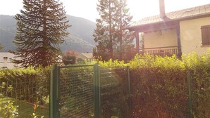 A fenced garden area with a house in the background, surrounded by greenery and mountains. - Charming 2-Room with Garden, Near Luchon, Sleeps 6, Pets Welcome, Private Parking (Montauban-de-Luchon)