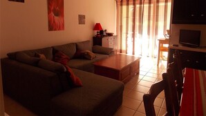A living room with a sofa, a coffee table, a TV, and a dining area with a table and chairs. - Charming 2-Room with Garden, Near Luchon, Sleeps 6, Pets Welcome, Private Parking (Montauban-de-Luchon)
