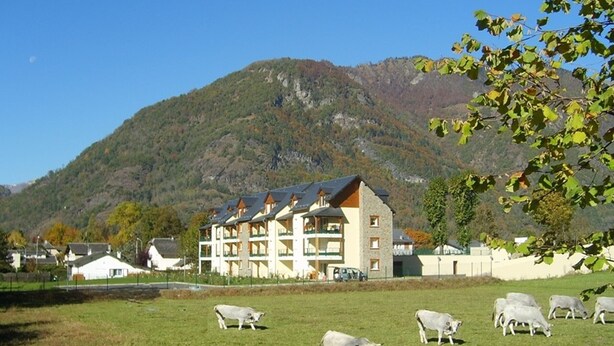 A hotel with multiple floors, a mountain backdrop, and a grassy field with grazing sheep. - Charming 2-Room with Garden, Near Luchon, Sleeps 6, Pets Welcome, Private Parking (Montauban-de-Luchon)