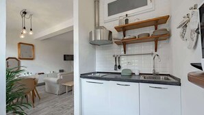 Eine moderne Küche mit weißen Schränken, einer Edelstahl-Spüle und einem eingebauten Backofen. Ein Essbereich mit weißem Tisch und Stühlen lädt zum Verweilen ein, und eine Pflanze steht in der Ecke.