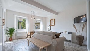 Ein modernes Wohnzimmer mit Sofa, Bank und Essbereich, einem an der Wand befestigten Fernseher und einem großen Fenster mit Aussicht.