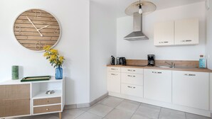 Une cuisine moderne avec des armoires blanches, une horloge ronde en bois, un luminaire suspendu et une petite plante posée sur le comptoir.
