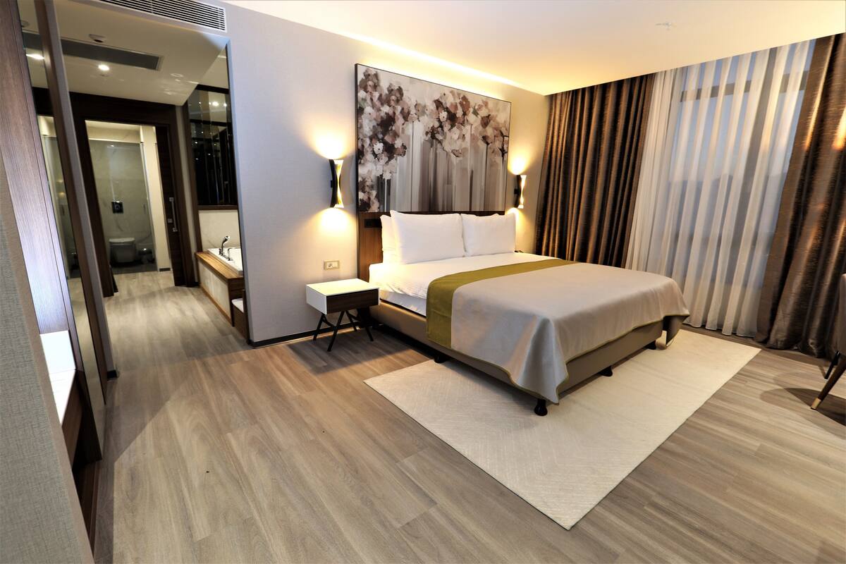 A modern hotel room with a large bed, bedside table, and a painting on the wall.