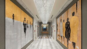 Un pasillo con piso de mármol, un banco central y dos grandes pinturas abstractas en las paredes.