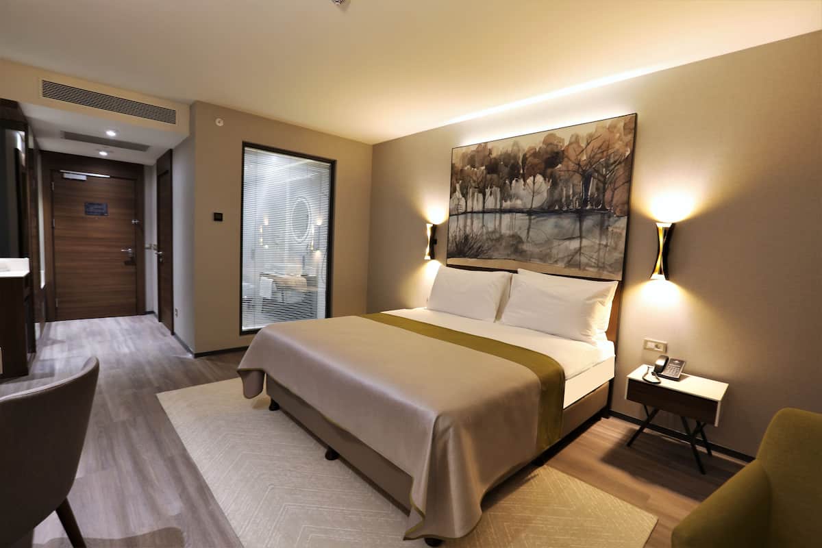 A hotel room with a large bed, a desk with a phone, and a chair.