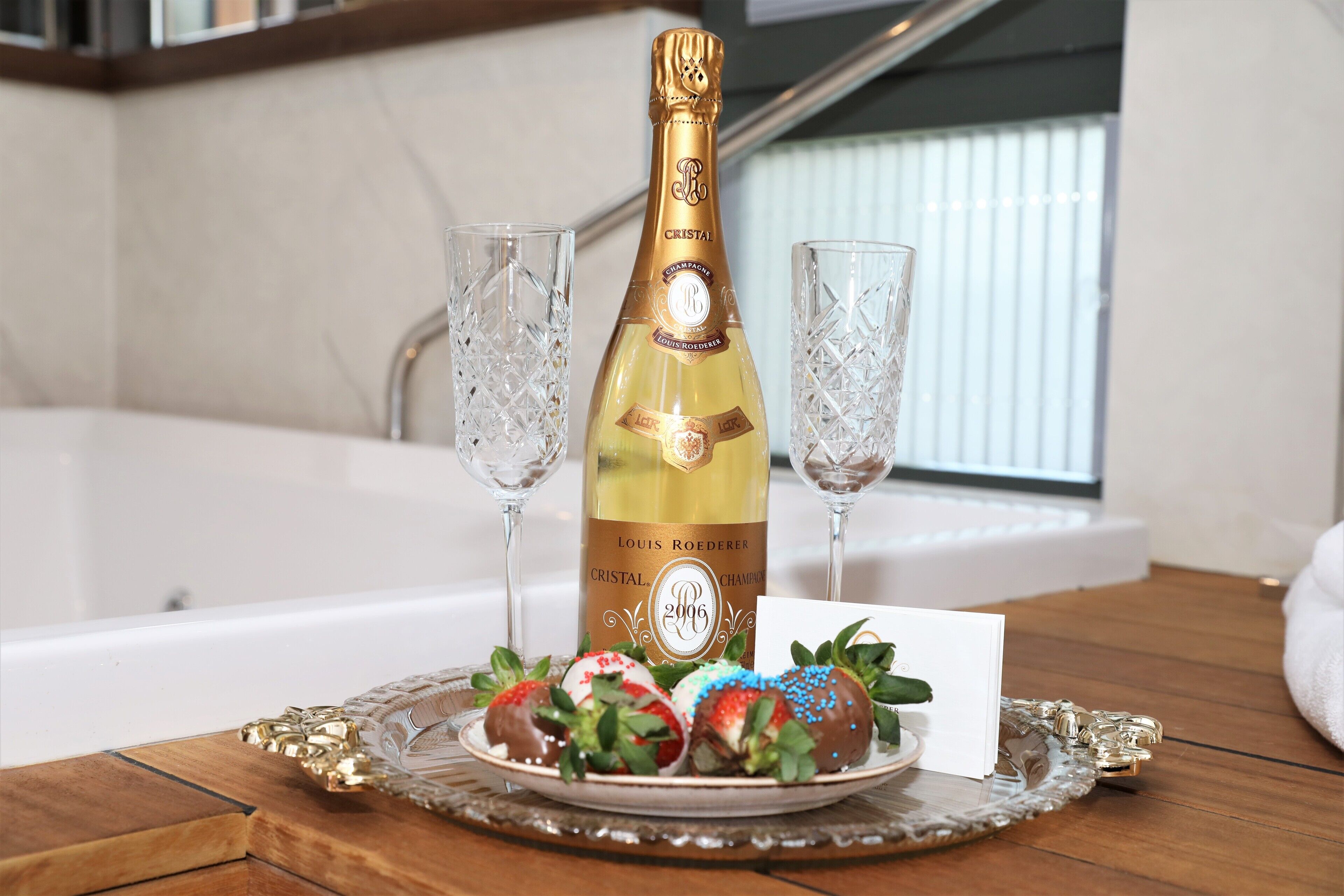 A bottle of Cristal champagne, two glasses, and chocolate-covered strawberries on a tray.