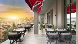 Una terraza moderna al aire libre con mesas y sillas, ventanas amplias y vistas de la ciudad.