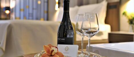Een fles Pinot Noir wijn, twee wijnglazen, een dienblad met een decoratieve bloem, en een visitekaartje op een houten tafel in een hotelkamer.