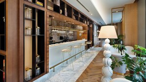 Un área de bar moderna con suelo de mármol, taburetes y una variedad de copas y botellas en estanterías.
