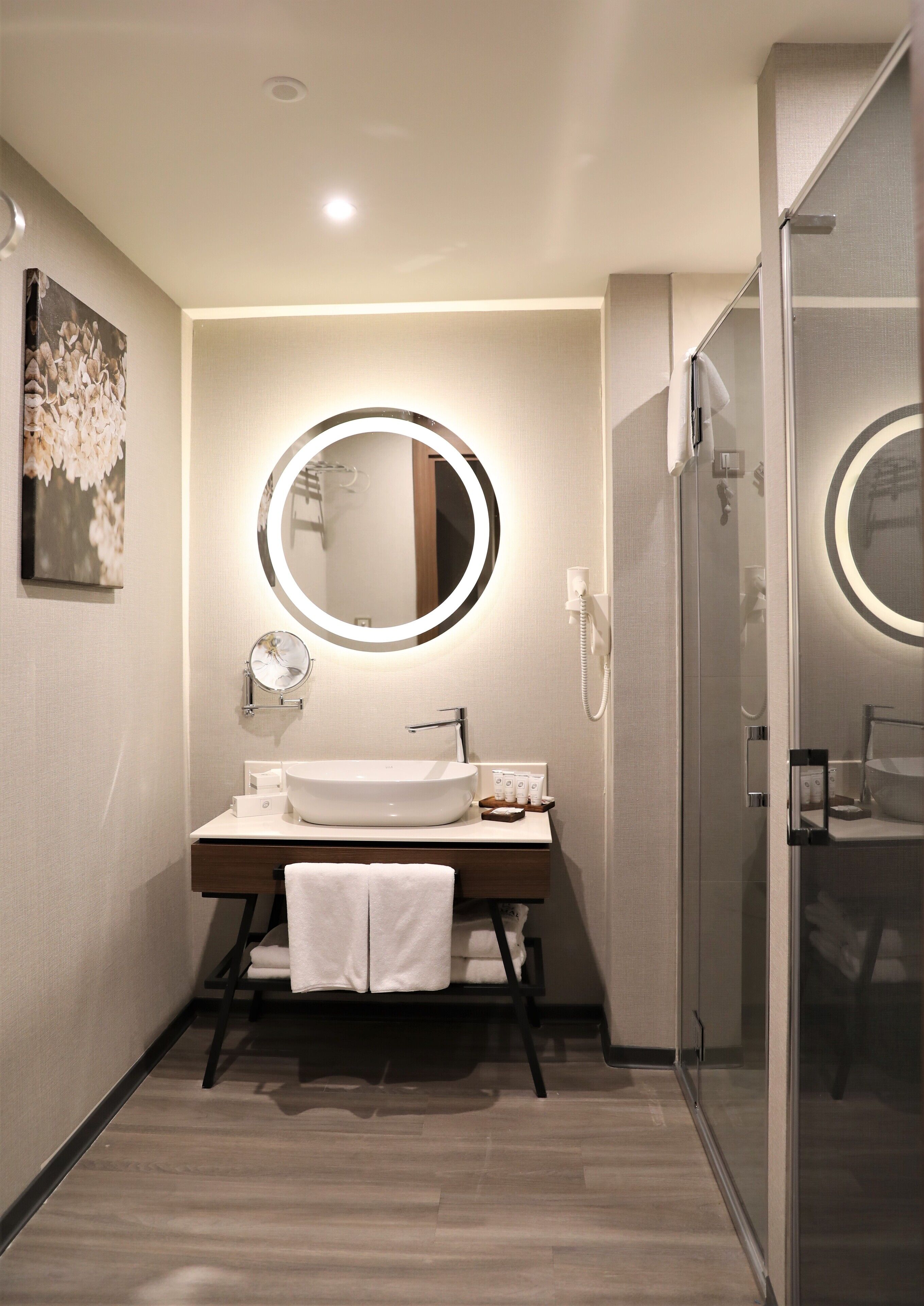 A modern bathroom with a white sink, a round mirror, and a glass shower enclosure.
