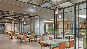 Un comedor amplio con varias mesas y sillas, ventanas grandes y luminarias modernas.