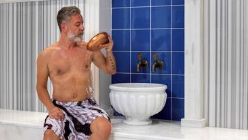 A man sitting on a white marble bench in a bathroom with a blue tiled wall and a white sink.