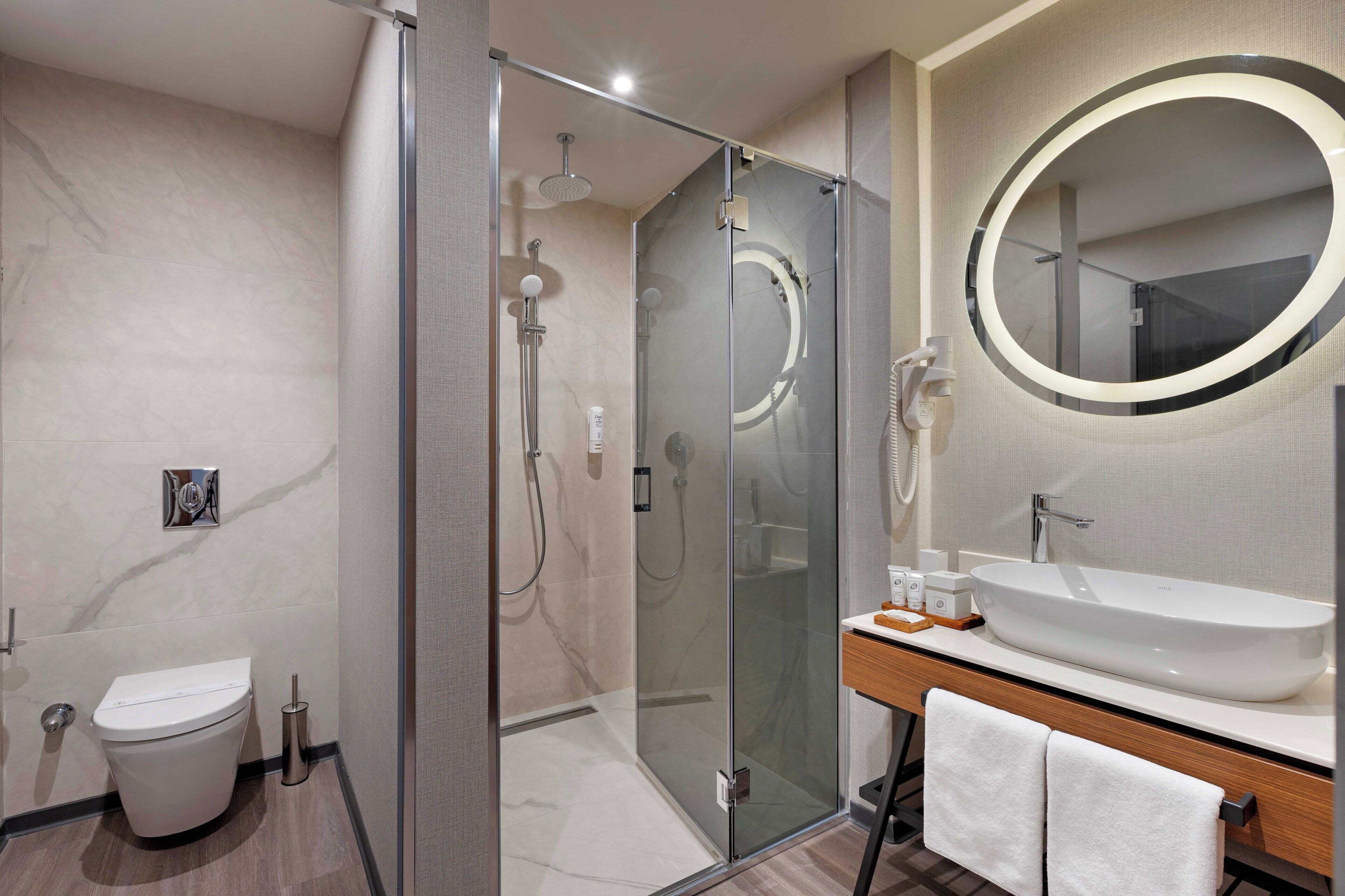 A modern bathroom with a glass-enclosed shower, a white sink, and a large mirror.