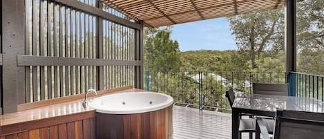 Una terraza de madera con un jacuzzi, una mesa y sillas.