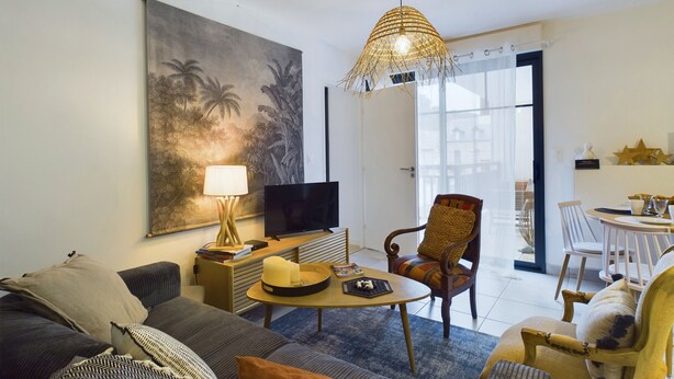 Una sala de estar con sofá, sillón, mesa de centro, televisor y un cuadro de paisaje tropical.