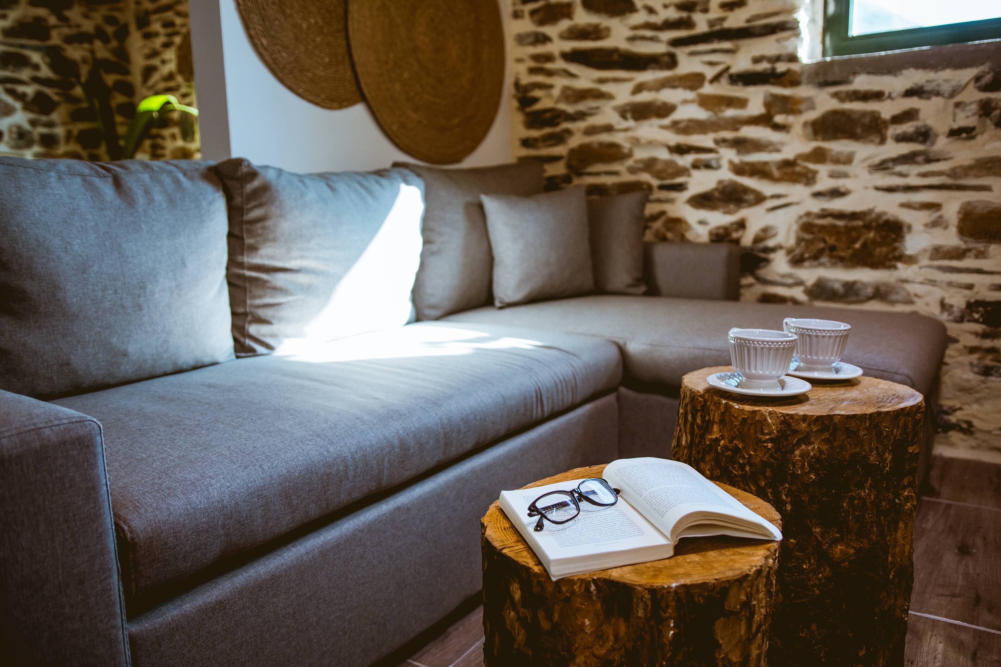 Una sala de estar moderna con un sofá gris, una mesa de centro de madera con un libro abierto y vasos, y una pared de piedra.