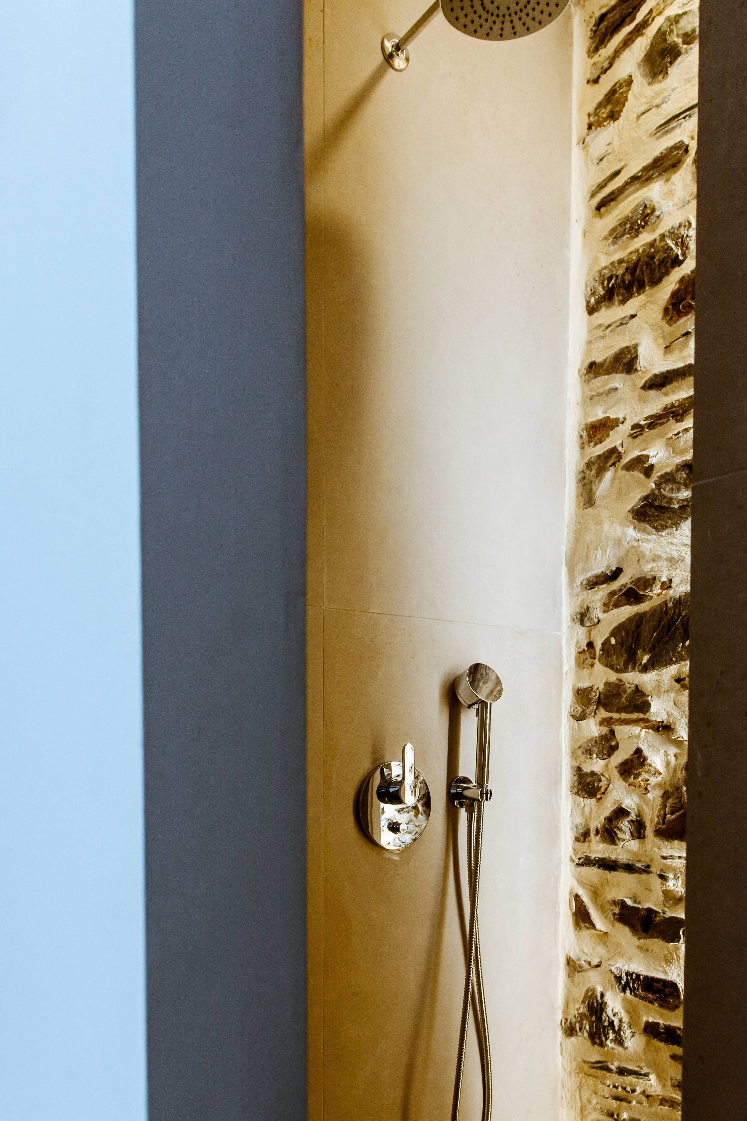 A shower with a stone wall, a metal showerhead, and a handheld shower attachment.
