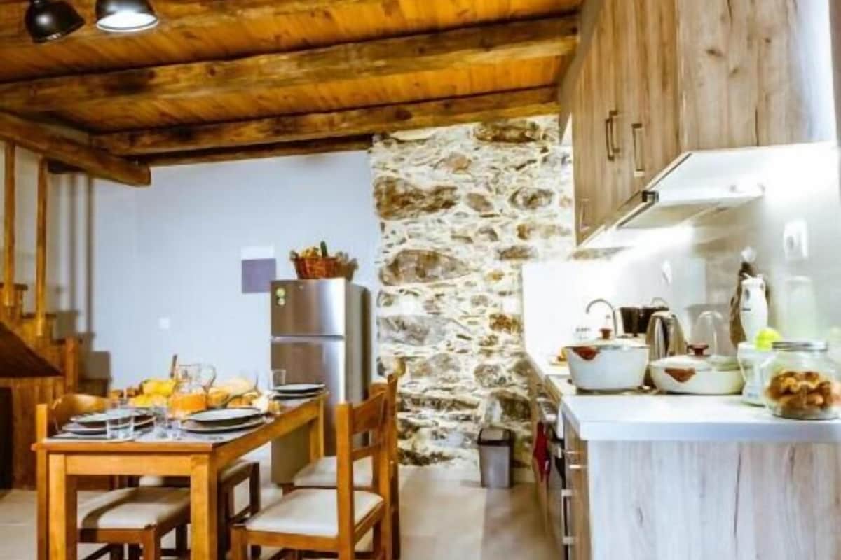 A rustic kitchen with wooden beams, a stone wall, and a dining area with a table set for four.