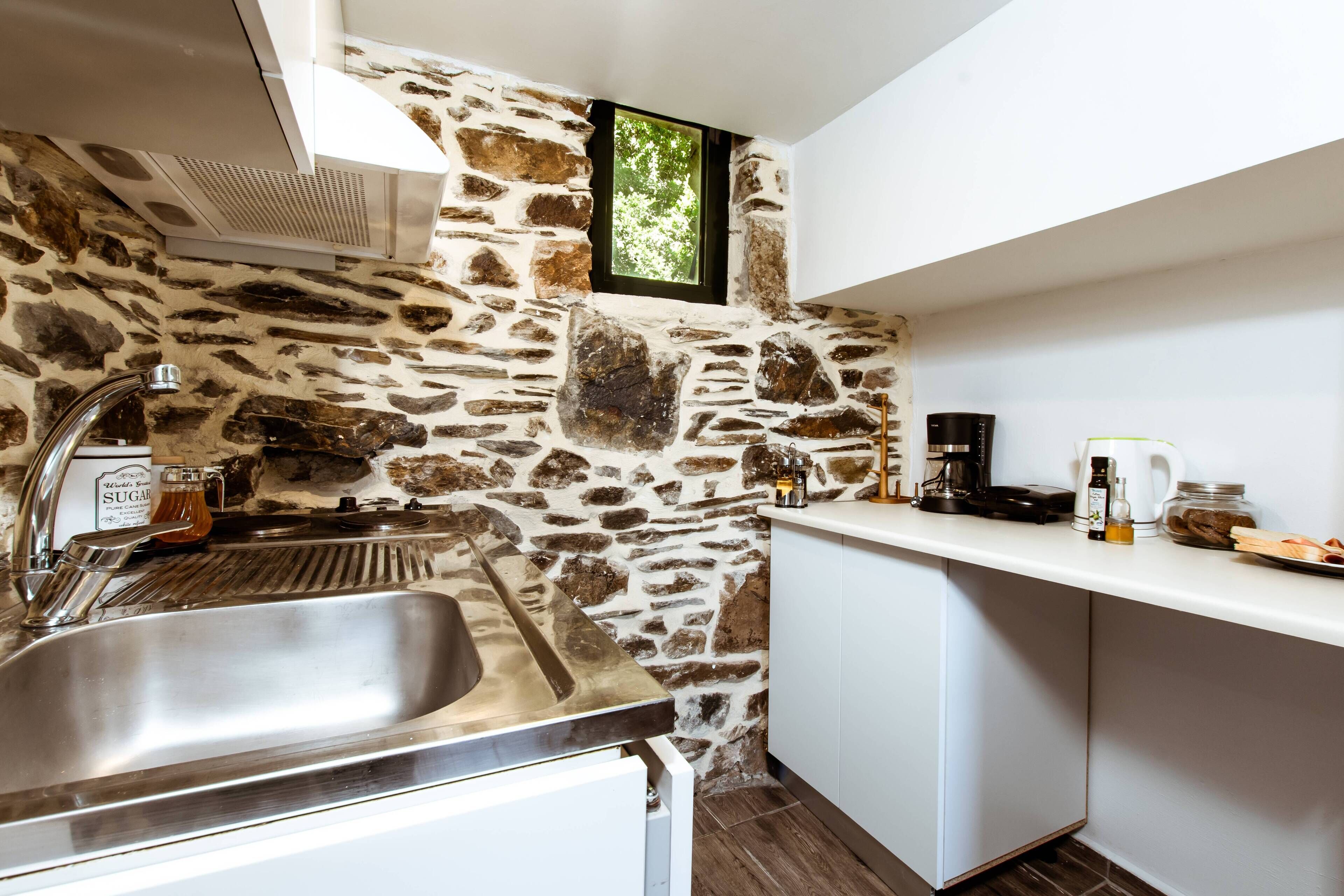 Una cocina con pared de piedra, pileta de acero inoxidable y encimera blanca.