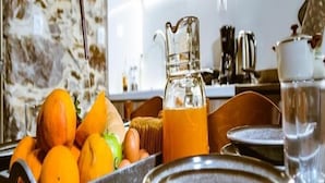 A breakfast setup with oranges, a pitcher of orange juice, and a coffee pot on a wooden table in a kitchen with stone walls. - Traditional Apartments Elafos (Kissamos)