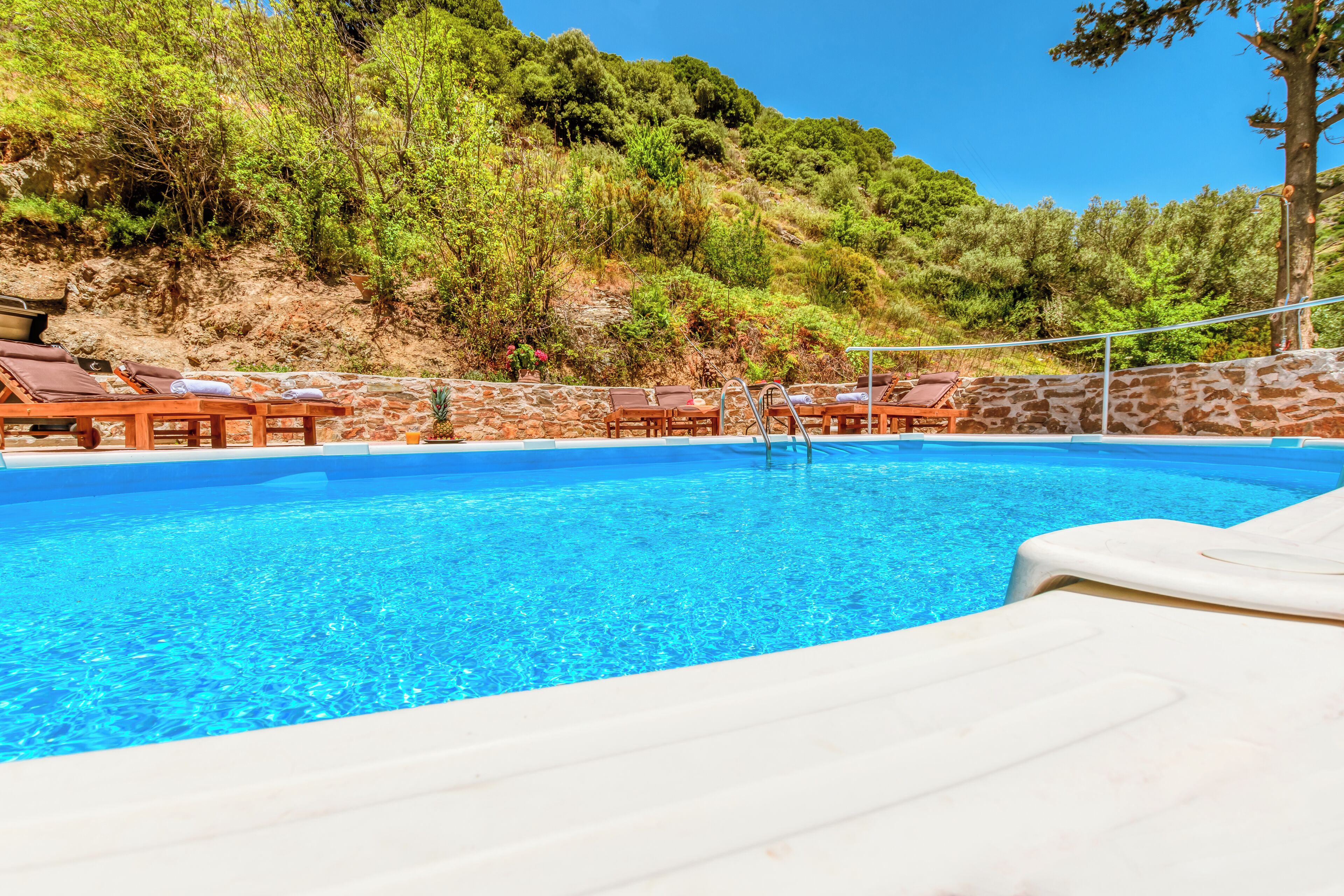 A swimming pool with lounge chairs and a stone wall.